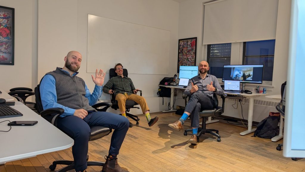 Three Four Eyes colleagues waving from their desks in the office